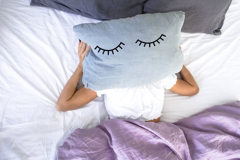Uma moça que dorme na cama branca não quer levantar-se cedo na manhã, cobrindo sua cara com o descanso com os olhos fechados nele fotos de stock Uma moça que dorme na cama branca não quer levantar-se cedo na manhã, cobrindo sua cara com o descanso com os olhos fechados nele fotos de stock