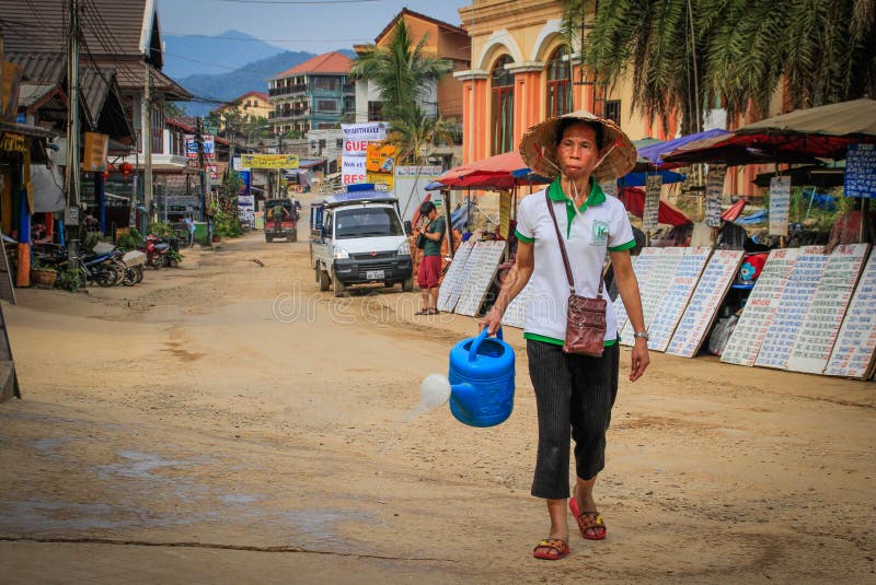 Uma mulher asiática russa com uma lata de água caminha à mão na rua da pequena cidade turística de Vang Vieng foto de stock Uma mulher asiática russa com uma lata de água caminha à mão na rua da pequena cidade turística de Vang Vieng foto de stock