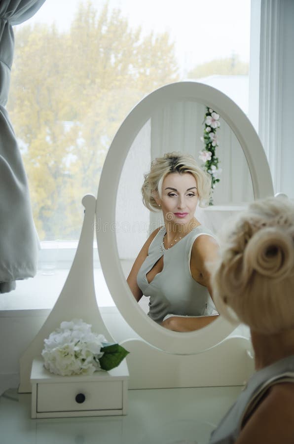Uma mulher bonita olha no espelho imagem de stock Uma mulher bonita olha no espelho imagem de stock