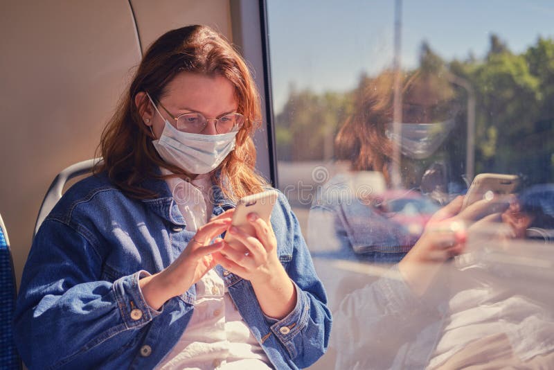 Uma mulher com máscara médica olha para a rota do ônibus em seu telefone Uma turista olha para os detalhes da viagem em seu smart