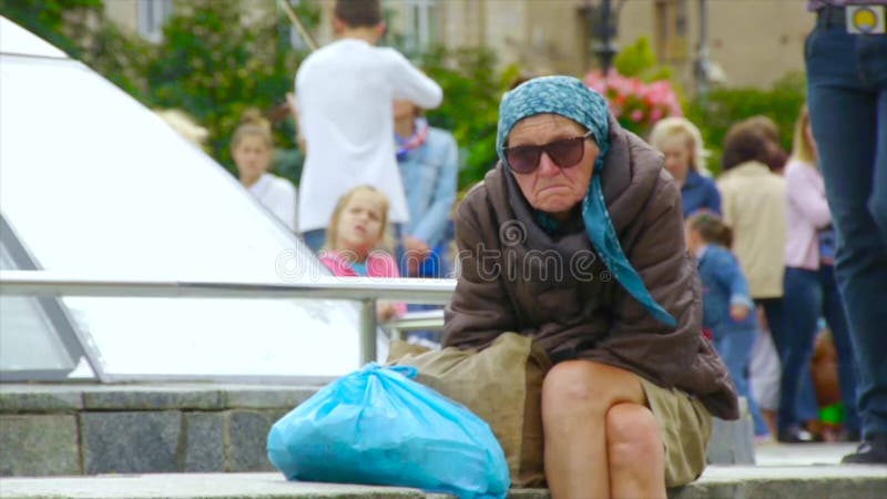 Uma mulher desabrigada bêbado está sentando-se na rua, ondulada acima