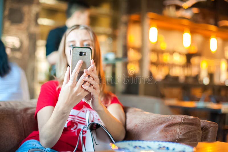 Uma mulher em um café em uma tabela faz o selfie no telefone Um visitante ao restaurante toma imagens dsi mesmo no telefone Mulhe fotografia de stock Uma mulher em um café em uma tabela faz o selfie no telefone Um visitante ao restaurante toma imagens dsi mesmo no telefone Mulhe fotografia de stock