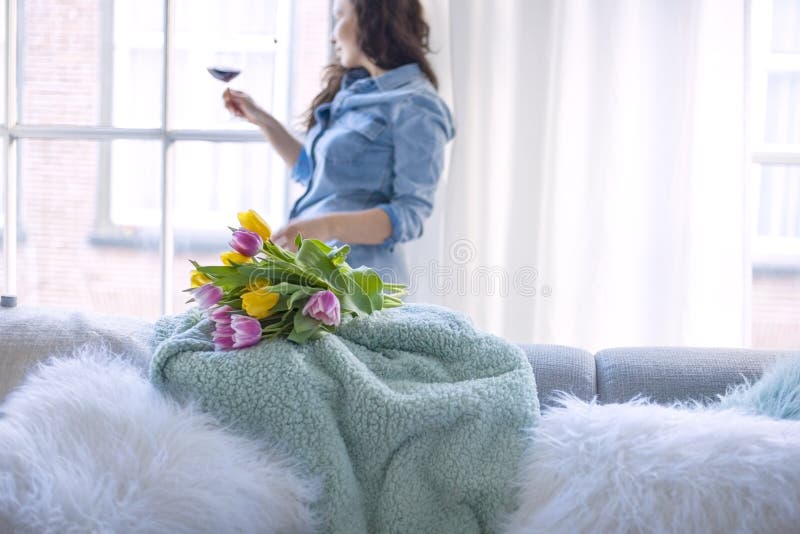 Uma mulher está guardando um vidro do vinho tinto e um ramalhete fresco de tulipas amarelas e cor-de-rosa Apenas chovido sobre Em foto de stock Uma mulher está guardando um vidro do vinho tinto e um ramalhete fresco de tulipas amarelas e cor-de-rosa Apenas chovido sobre Em foto de stock