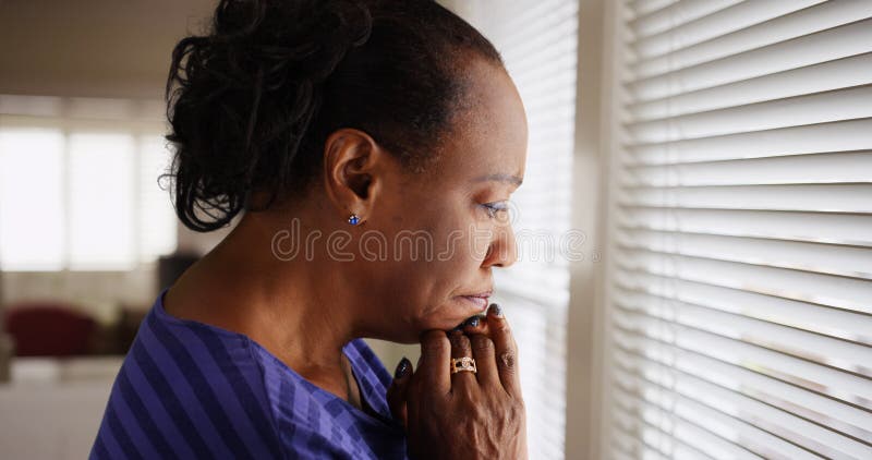 Uma mulher negra mais idosa olha tristemente para fora sua janela