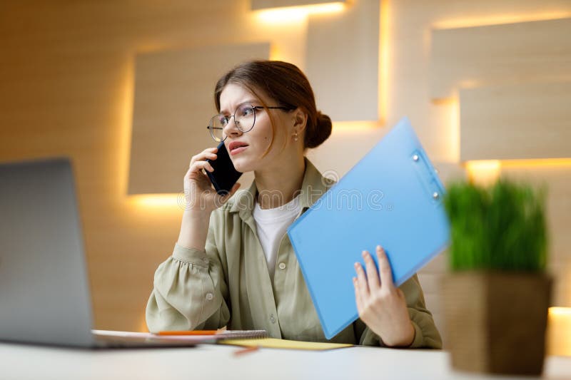 Uma mulher no escritório está falando ao telefone com uma pasta em suas mãos no local de trabalho discutindo os detalhes do contra
