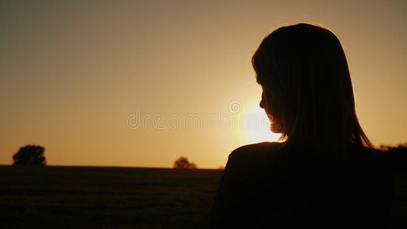 Uma mulher pensativa olha o sol de ajuste, a vista traseira Os sonhos e o conceito da solidão, olham para a frente foto de stock Uma mulher pensativa olha o sol de ajuste, a vista traseira Os sonhos e o conceito da solidão, olham para a frente foto de stock