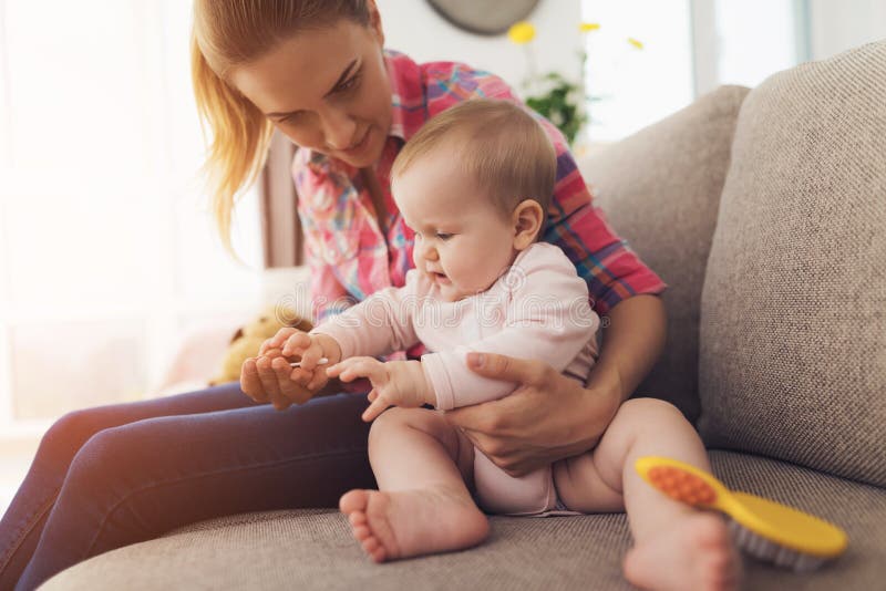 Uma mulher senta-se no sofá e limpa-se seus pregos A criança gosta de quando a mamã toca em seus dedos fotografia de stock Uma mulher senta-se no sofá e limpa-se seus pregos A criança gosta de quando a mamã toca em seus dedos fotografia de stock