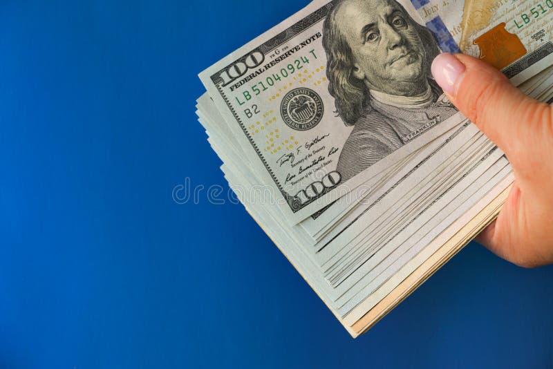 Uma multidão de notas de cem dólares guardadas na mão contra um fundo azul brilhante. o conceito de dinheiro a pagar pelo pagament