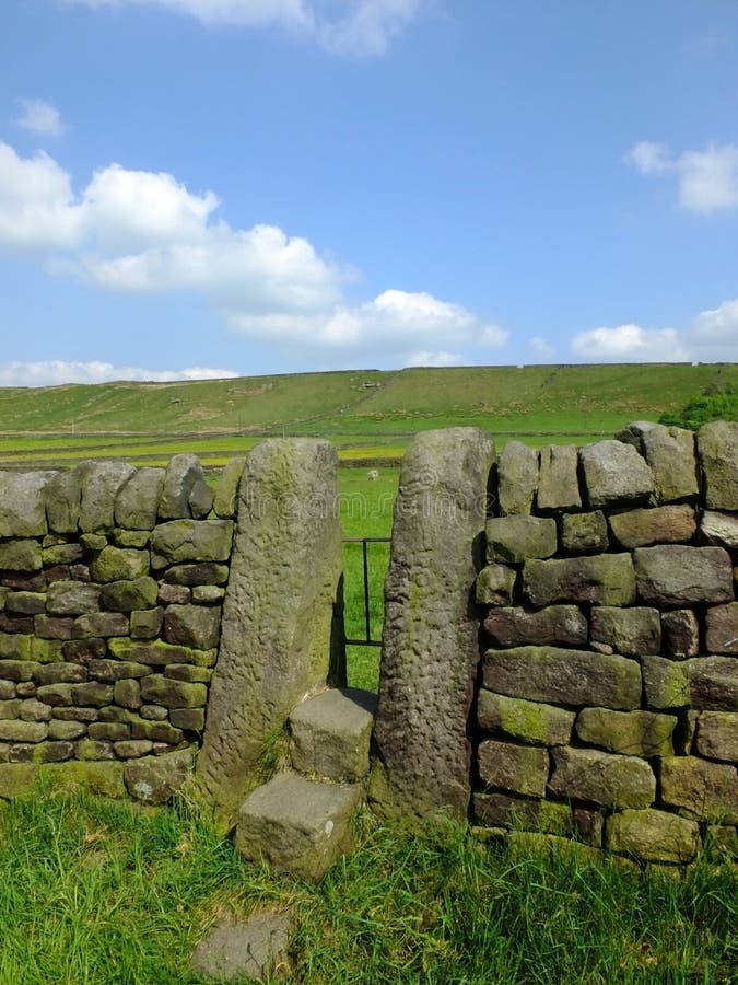 Uma parede de pedra seca com escada de pedra ou porta estreita com etapas em um prado do montanhês dos vales de yorkshire com um