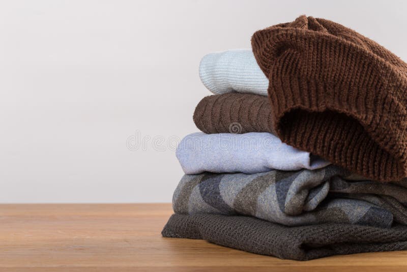 Uma pilha de camisetas mornas em uma tabela de madeira em um fundo claro Roupa do inverno foto de stock royalty free Uma pilha de camisetas mornas em uma tabela de madeira em um fundo claro Roupa do inverno foto de stock royalty free