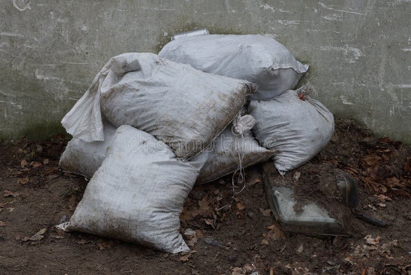 Uma pilha dos sacos de lixo brancos na terra perto da cerca fotografia de stock Uma pilha dos sacos de lixo brancos na terra perto da cerca fotografia de stock
