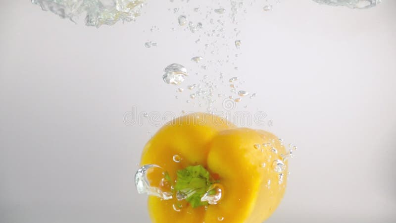 Uma pimenta amarela cai na água com salpicos e bolhas em câmera lenta. legume em fundo branco isolado.