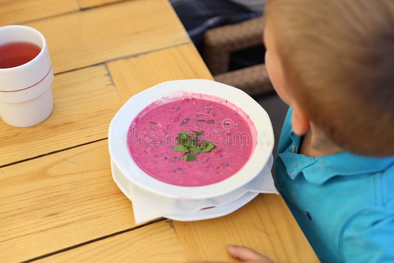Uma placa branca com sopa grossa cor-de-rosa na frente de um menino da criança imagem de stock