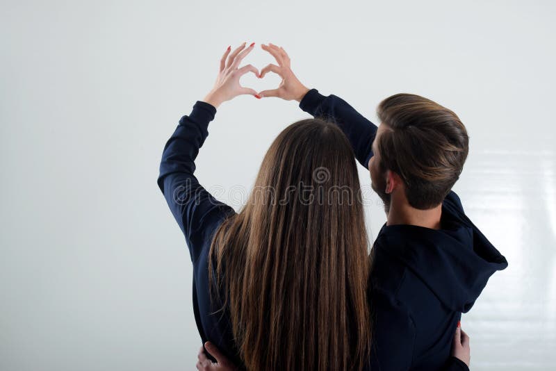 Uma posição nova dos pares que olha para trás a parede branca mostra ao coração fotos de stock royalty free Uma posição nova dos pares que olha para trás a parede branca mostra ao coração fotos de stock royalty free