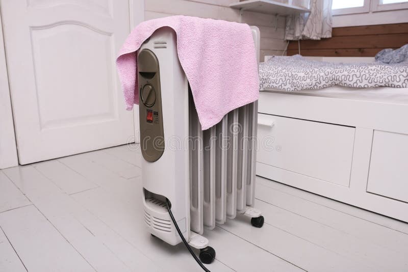 Uma situação perigosa com o aquecedor móvel de óleo coberto com uma toalha que está seca num dispositivo elétrico quente
