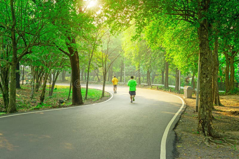 Uma trilha movimentando-se concreta do asfalt preto em um parque público, dois pessoas que vestem a camisa amarela e verde de T q foto de stock Uma trilha movimentando-se concreta do asfalt preto em um parque público, dois pessoas que vestem a camisa amarela e verde de T q foto de stock