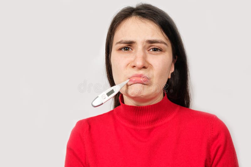 A sad sick woman with a thermometer in her mouth looks into the camera, copying space for text. A sad sick woman with a thermometer in her mouth looks into the camera, copying space for text