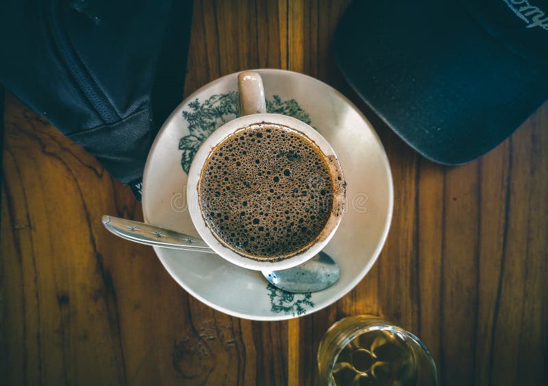 Só o café pode me refrescar. mulher afro-americana sonolenta e cansada  cobre metade do rosto com a palma da mão, tem expressão triste, fecha os  olhos, carrega um copo descartável de bebida com cafeína, continua  trabalhando.