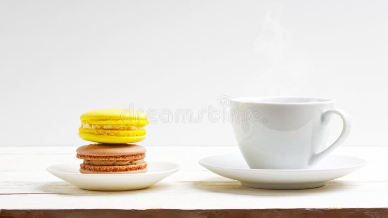 Uma xícara de café e dois macarões limão e chocolate em mesa de madeira branca imagem de stock royalty free Uma xícara de café e dois macarões limão e chocolate em mesa de madeira branca imagem de stock royalty free
