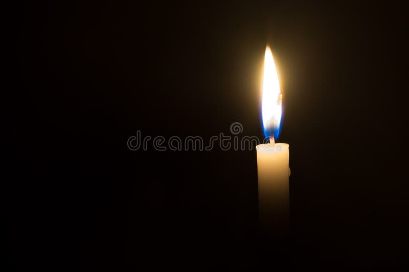 Uma única luz da vela que incandesce em uma vela branca no fundo preto