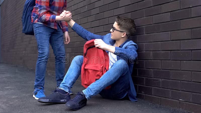 Kind teenage student giving helping hand to bullied nerd boy, supportive friend, stock photo. Kind teenage student giving helping hand to bullied nerd boy, supportive friend, stock photo