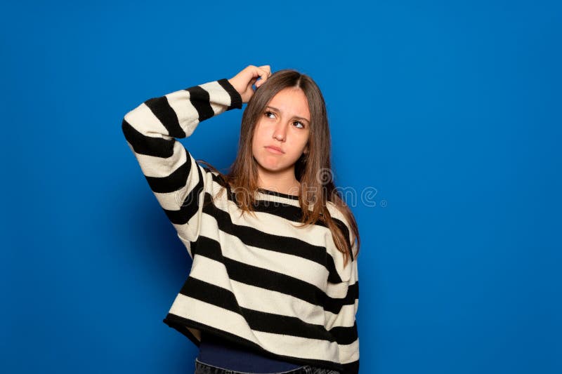 Un'adolescente ispanica di circa 15 anni indossa un maglione a strisce e un'espressione facciale sconcertata la gratta immagine stock