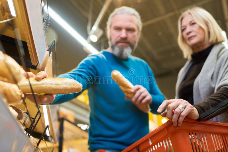 Un adulto cliente maschio prende due baguette di frumento fresco dallo scaffale del supermercato immagine stock libera da diritti
