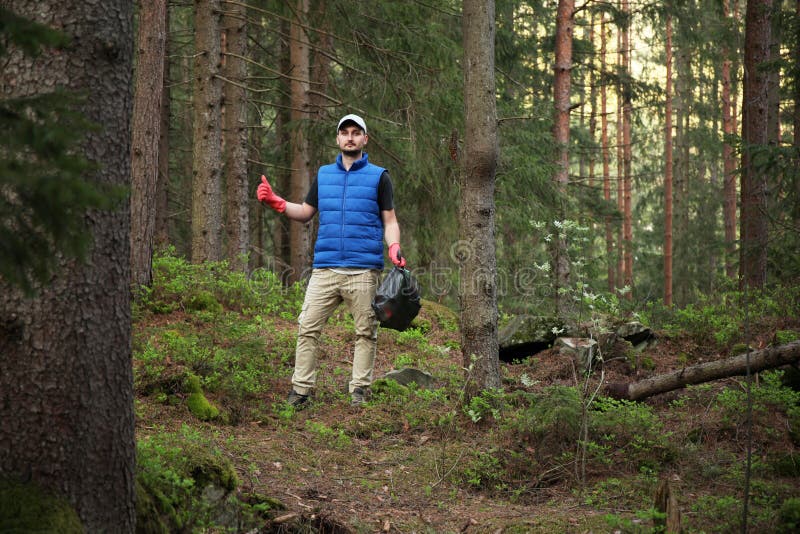 Adult man volunteer in red gloves removes plastic trash in forest, caring for environment. Adult man volunteer in red gloves removes plastic trash in forest, caring for environment.