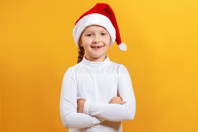 Un affascinante ritratto di una bambina carina felice col cappello di santa Il bambino ha incrociato le braccia e guarda la telec fotografie stock Un affascinante ritratto di una bambina carina felice col cappello di santa Il bambino ha incrociato le braccia e guarda la telec fotografie stock