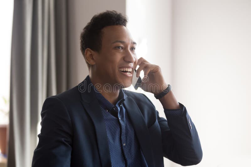 Un alegre hombre de negocios de raza mixta que habla por teléfono móvil se siente muy feliz fotografía de archivo