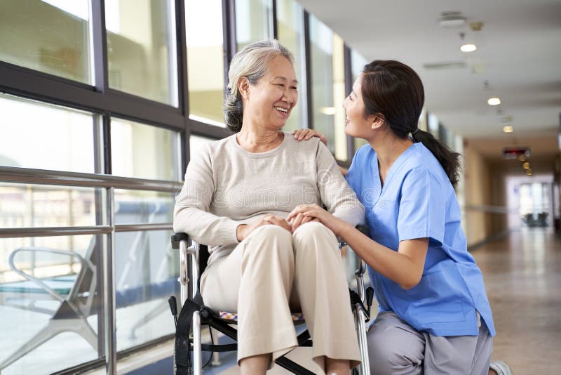 Friendly staff caregiver of nursing home talking to asian senior woman in hallway. Friendly staff caregiver of nursing home talking to asian senior woman in hallway