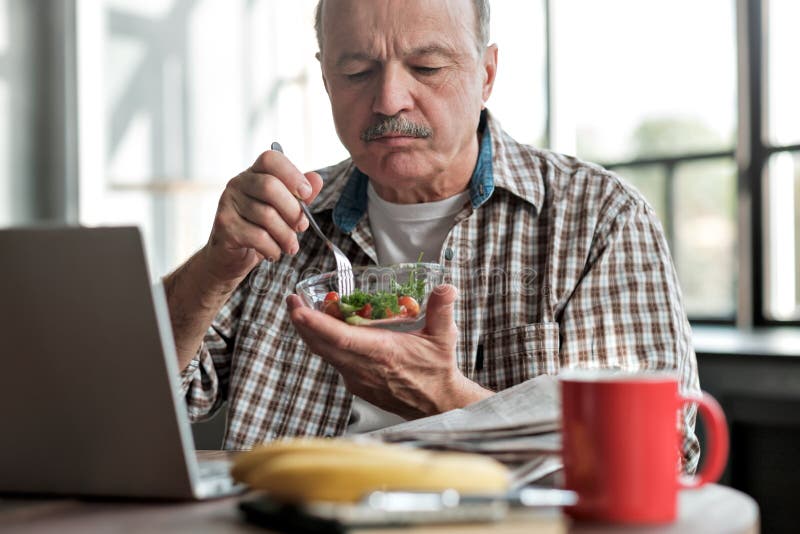 Un anciano hispano comiendo ensalada fresca por la mañana sentado en el salón fotografía de archivo Un anciano hispano comiendo ensalada fresca por la mañana sentado en el salón fotografía de archivo