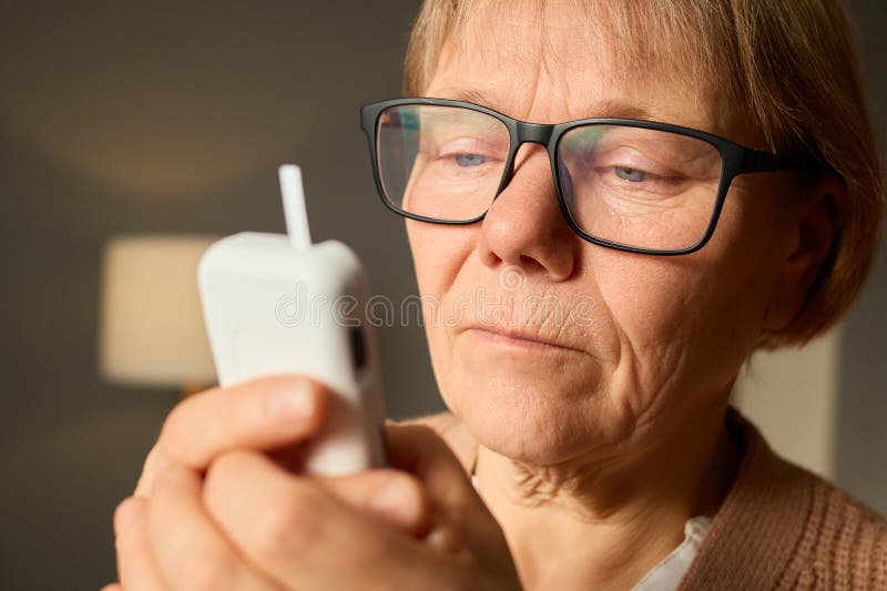 Un'anziana donna è seduta al telefono mentre si siede al chiuso per sottolineare il suo impegno tecnologico in una fotografia stock libera da diritti