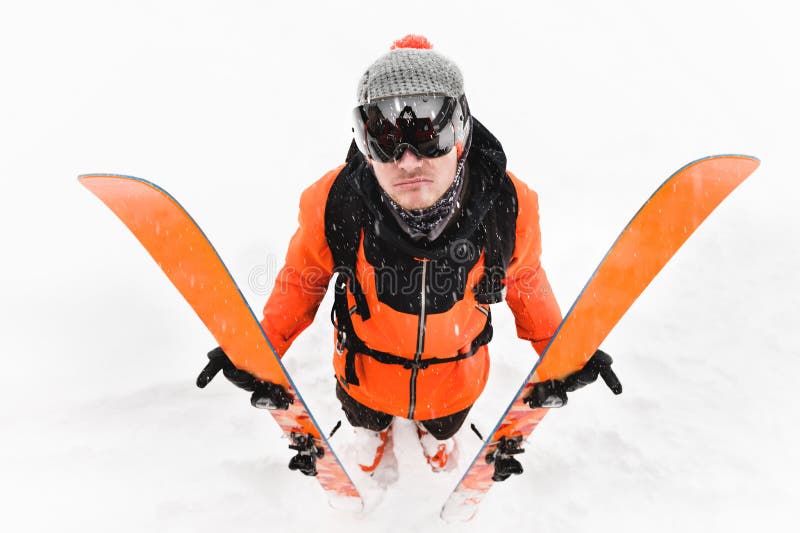 Un atleta professionista dello sciatore in un vestito nero arancio con una passamontagna nera con gli sci nei suoi supporti delle immagini stock libere da diritti Un atleta professionista dello sciatore in un vestito nero arancio con una passamontagna nera con gli sci nei suoi supporti delle immagini stock libere da diritti