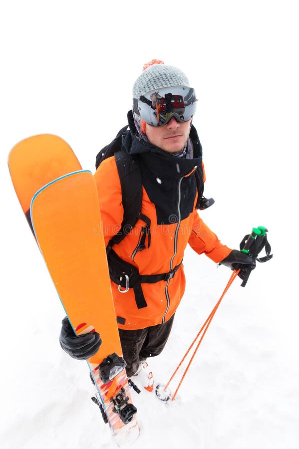 Un atleta professionista dello sciatore in un vestito nero arancio con una passamontagna nera con gli sci nei suoi supporti delle immagini stock Un atleta professionista dello sciatore in un vestito nero arancio con una passamontagna nera con gli sci nei suoi supporti delle immagini stock
