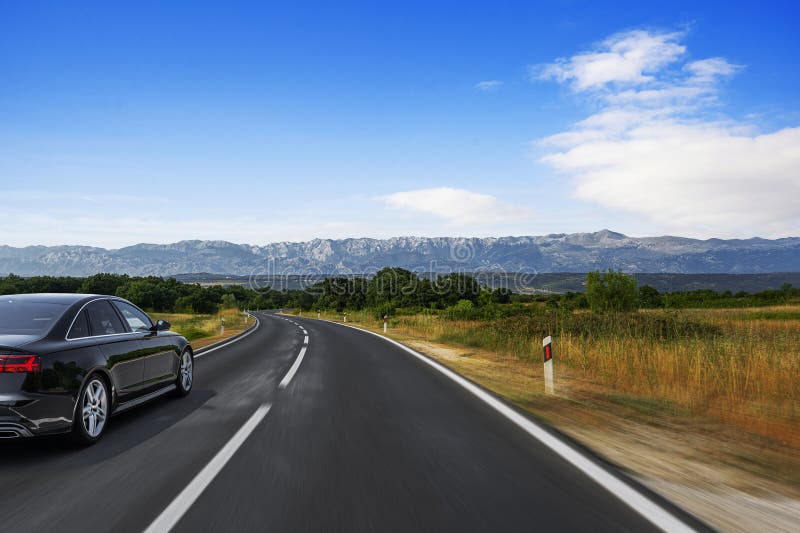 Un'auto nera elegante accelera lungo un'autostrada che attraversa la campagna fotografia stock