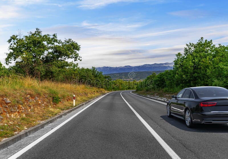 Un'auto nera elegante guida lungo una tortuosa strada rurale fotografia stock libera da diritti