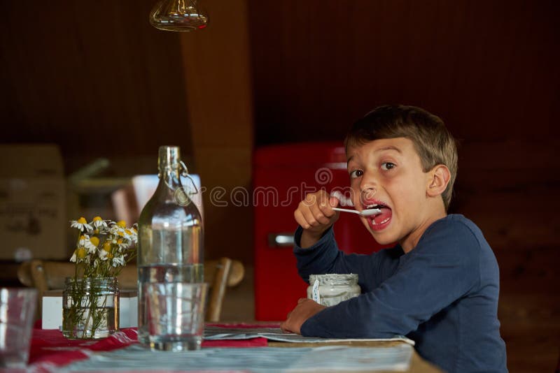 Un bambino dell'asilo mangia del gelato in cucina. camomilla in vaso trasparente. fotografia stock