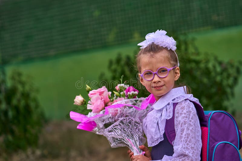 Un bambino della ragazza in uniforme scolastico con gli archi, i vetri e una borsa di scuola sul suo indietro va alla prima class immagini stock Un bambino della ragazza in uniforme scolastico con gli archi, i vetri e una borsa di scuola sul suo indietro va alla prima class immagini stock