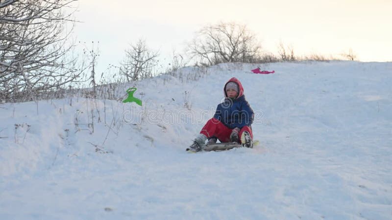 Un bambino felice guida una slitta lungo un pendio di neve. archivi video