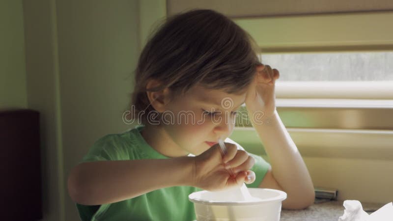 Un bambino mangia il pranzo seduto in un compartimento ferroviario mentre viaggia e pulisce la bocca con un tovagliolo di carta.