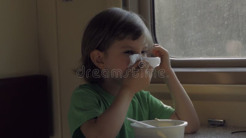 Un bambino mangia il pranzo seduto in un compartimento ferroviario mentre viaggia e pulisce la bocca con un tovagliolo di carta.