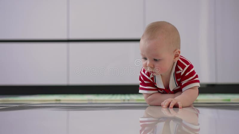 Un bambino piccolo striscia sul pavimento. allenamento di neonato per la prima volta. un ragazzino impara a strisciare sulle piast