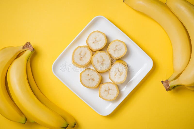Un banch de plátanos y de un plátano cortado en un plato sobre el CCB amarillo fotografía de archivo Un banch de plátanos y de un plátano cortado en un plato sobre el CCB amarillo fotografía de archivo