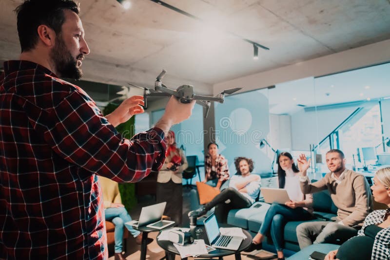 Un barbu dans un bureau moderne qui explique à sa jeune équipe diversifiée comment un drone travaille images stock