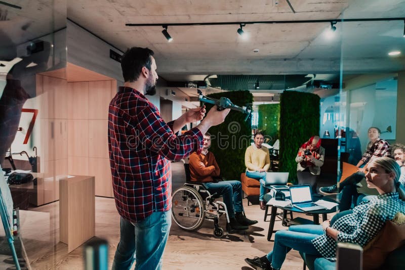 Un barbu dans un bureau moderne qui explique à sa jeune équipe diversifiée comment un drone travaille photo stock