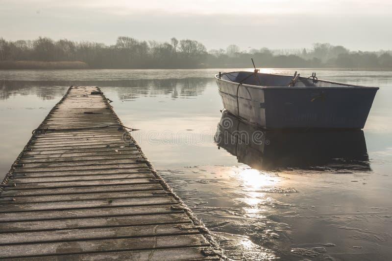 Un barco que rema flota a la deriva en un lago congelado al lado de una calzada vacía imagen de archivo libre de regalías Un barco que rema flota a la deriva en un lago congelado al lado de una calzada vacía imagen de archivo libre de regalías