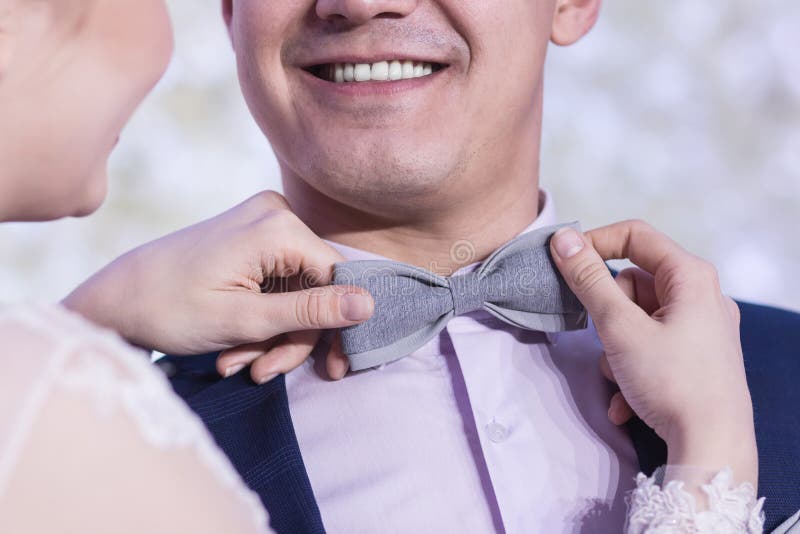 Un beau sourire d'un type dans un costume bleu, quand les mains du ` s de fille ajustent le noeud papillon gris images stock Un beau sourire d'un type dans un costume bleu, quand les mains du ` s de fille ajustent le noeud papillon gris images stock