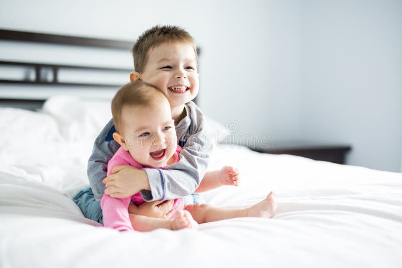Un bebé y su hermano en la cama que se divierte foto de archivo Un bebé y su hermano en la cama que se divierte foto de archivo