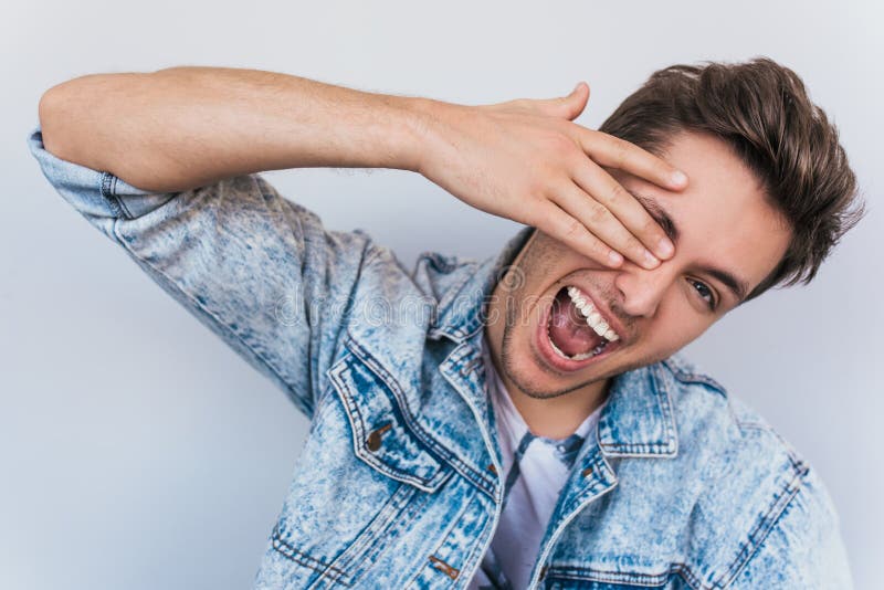 Un bel giovane che si nasconde in faccia con le mani e gli fa vedere. ritratto di occhi di copertura positivi fotografia stock